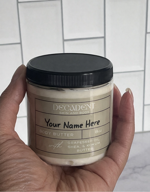 Hand holding a jar of body butter with a customizable label against a tiled wall background